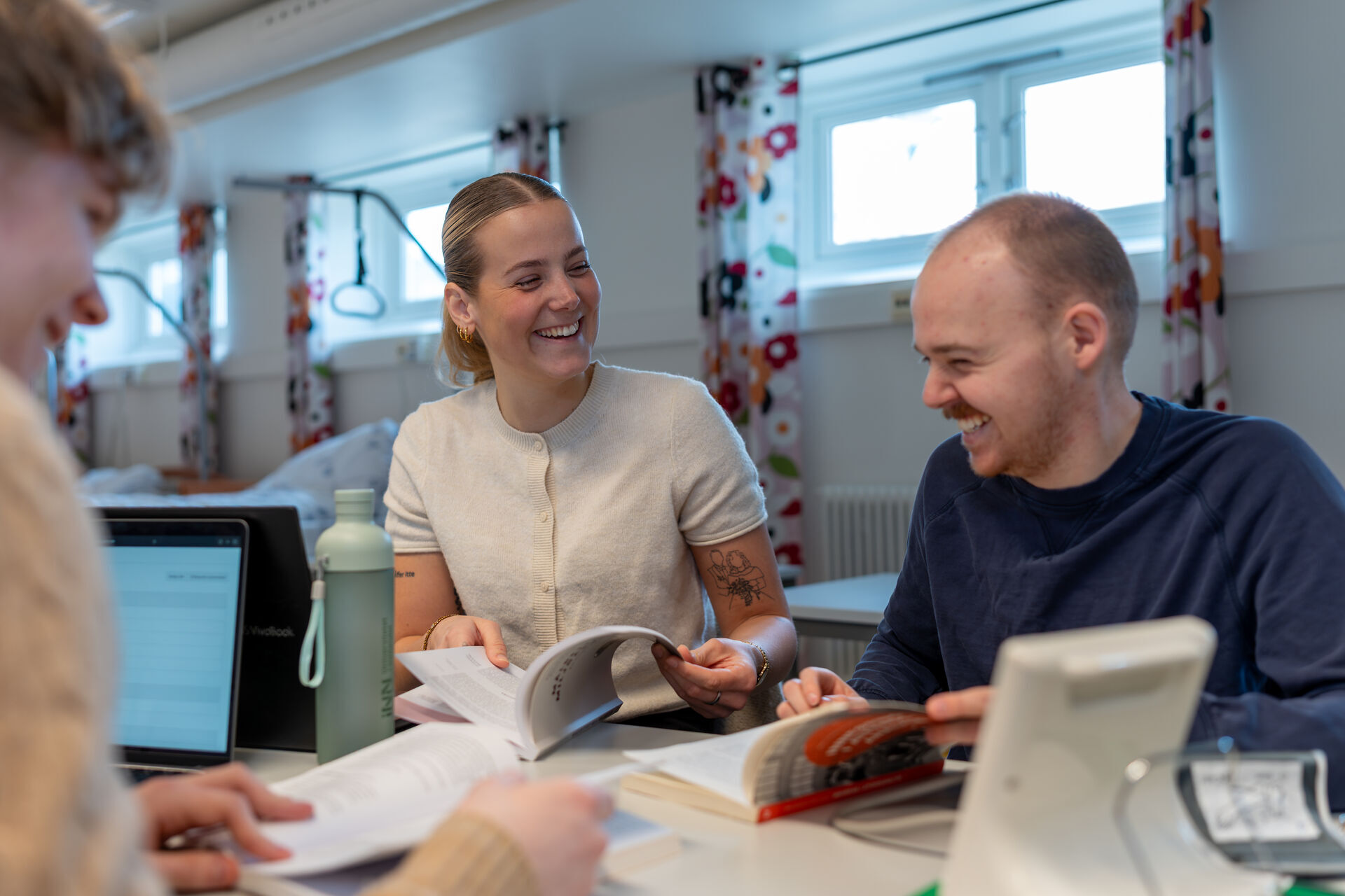 Studenter sitter i øvingslokalet vernepleie og jobber med oppgaver. En jente og to gutter.