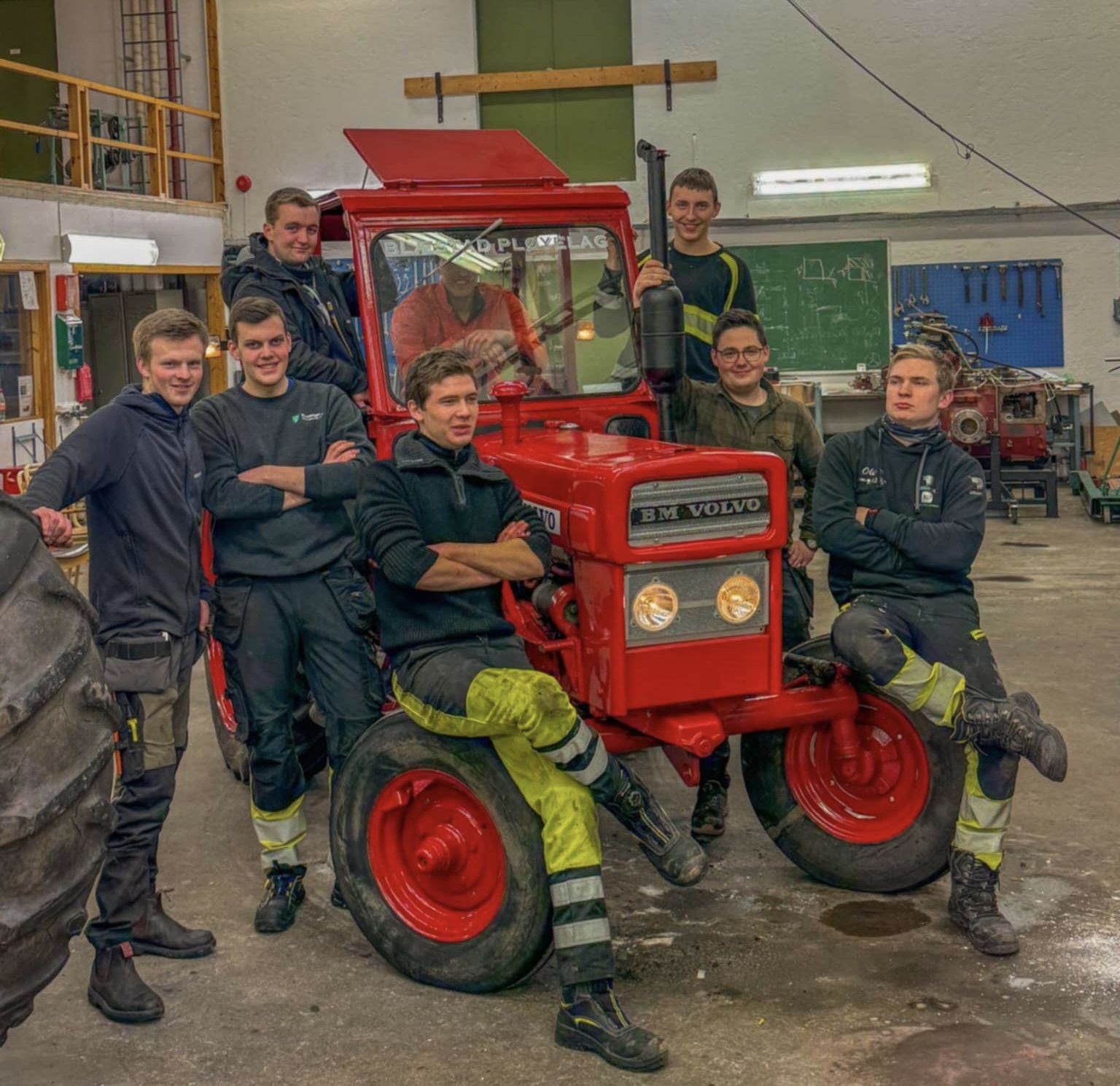Gutter som står rundt en rød traktor i et verksted