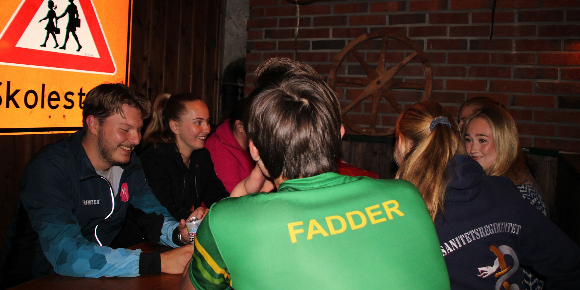 En gruppe studenter sitter rundt et bord i Bodegaen under fadderuka og prater sammen under fadderuka. Stemningen er sosial og hyggelig, med både latter og smil.